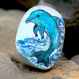 Hand crafted painted dolphin porpoise rock blue white background ocean waves